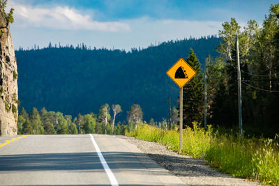 Road sign by trees against sky