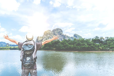 Rear view of man standing at riverbank against sky