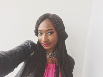 Portrait of young woman with braided hair standing by white wall