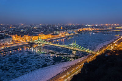 Aerial view of bridge over river with cityscape in background at night