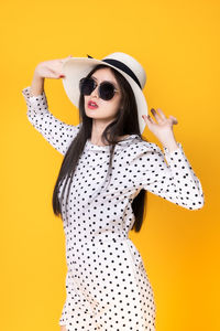 Young woman wearing sunglasses standing against yellow background