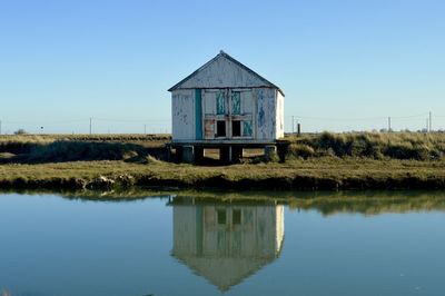 Built structure by lake against clear blue sky