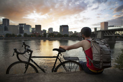 Athlete carrying backpack while sitting on retaining wall by lake