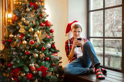 Teenage boy in santa's hat sits in a christmas-decorated room and chats online. 