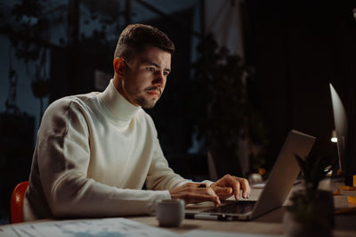 Focused man using laptop for work and trying hurry up to deadline while sitting in the modern office