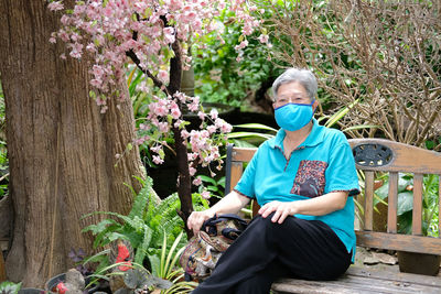 Portrait of woman wearing mask sitting by potted plant outdoors