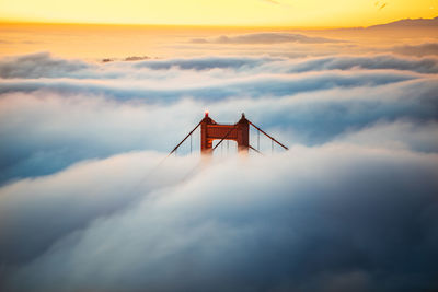 Golden gate bridge peak during fog season against sky during sunset