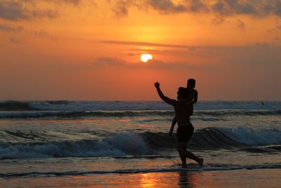 Silhouette of father and son at beach against sky during sunset