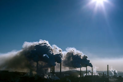 Smoke emitting from factory against sky on sunny day