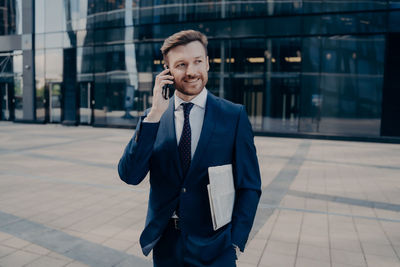 Smiling businessman talking on phone while standing outdoors