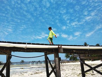 Full length of boy walking on pier at beach against sky