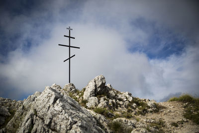 Low angle view of cross on peak against cloudy sky