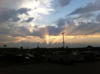 Cars on road against cloudy sky at sunset