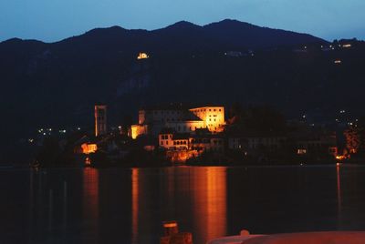 Illuminated buildings by sea against sky at night