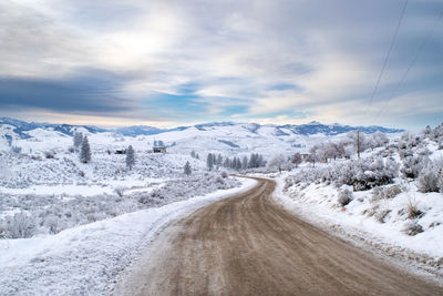 Road passing through snow covered landscape against sky