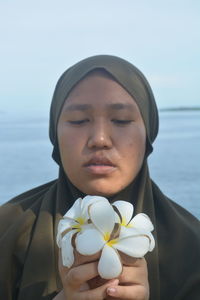 Portrait of mid adult woman holding flower against sea