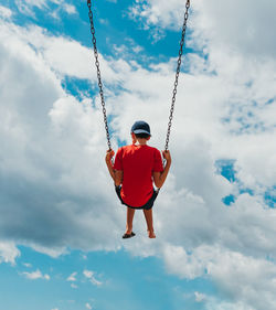 Rear view of boy on a swing with only cloudy sky in the background.