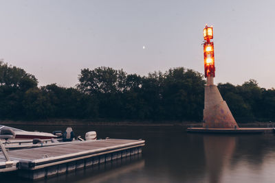 Lighthouse by lake against sky at sunset