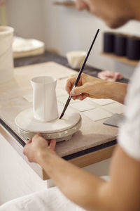 Young male worker painting pottery in crockery workshop