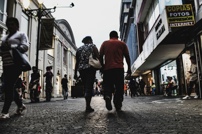 Rear view of people walking on road along buildings