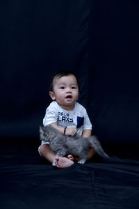 Full length of cute baby girl sitting against black background