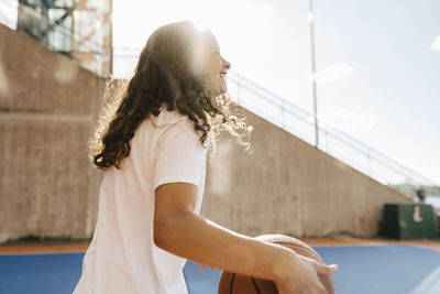 Smiling girl with ball at basketball court on sunny day