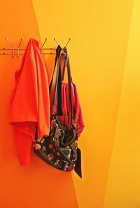 Clothes and shoulder bag hanging on yellow wall at home