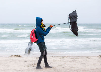 Full length of woman holding umbrella at beach during rainy season