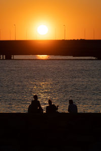 Silhouette people looking at sea against sky during sunset