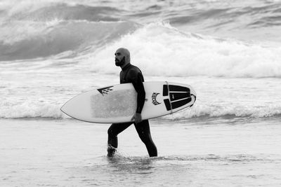 Rear view of man holding surfboard on beach
