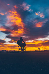 Silhouette man riding bicycle on road against sky during sunset