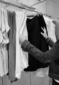 Midsection of person choosing clothes hanging on rack in store