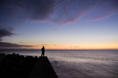 Silhouette man standing at beach against sky during sunset