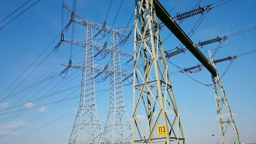 Low angle view of electricity pylon against blue sky
