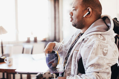 Disabled man with drink sitting on wheelchair at home