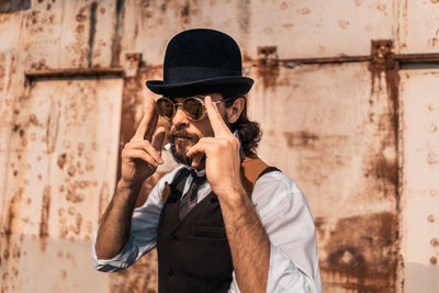 Man holding camera while standing against wall