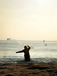 Rear view of woman standing at beach against sky
