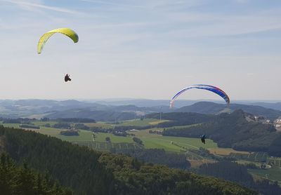 People paragliding over landscape against sky