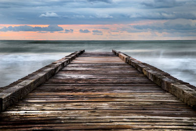 Wooden pier over sea against sky during sunset