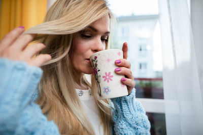 A woman drinks hot tea from a mug and combs her hair.