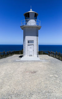 Lighthouse by sea against clear blue sky