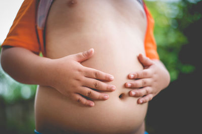 Midsection of boy touching his stomach outdoors