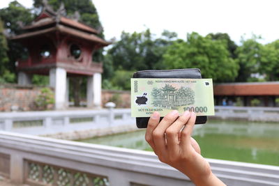 Cropped hand of person holding paper currency against pond