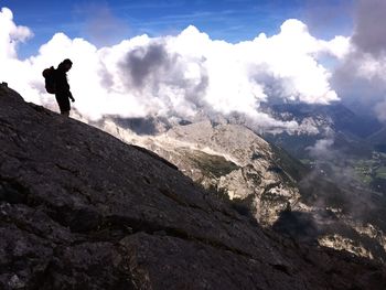 Hiker standing on rocky mountains against cloudy sky