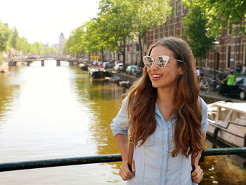 Portrait of smiling young woman standing by canal