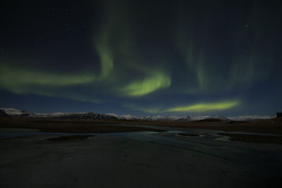 Low angle view of aurora borealis over mountains and lake