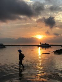 Silhouette man standing in sea against sky during sunset