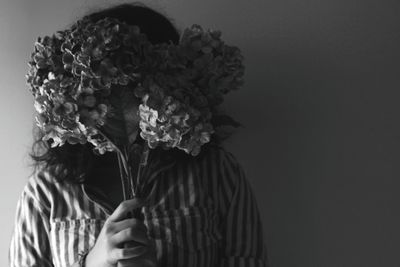 Woman with face covered by flowers standing against wall
