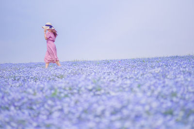 Surface level shot of woman standing amidst purple flowers on field against sky