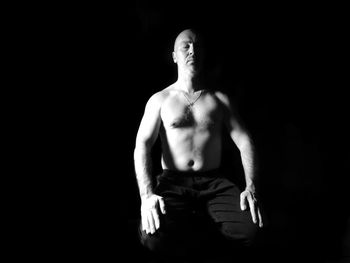 Shirtless man sitting with eyes closed against black background